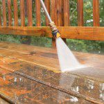 A person cleaning the wooden deck with a power washer.