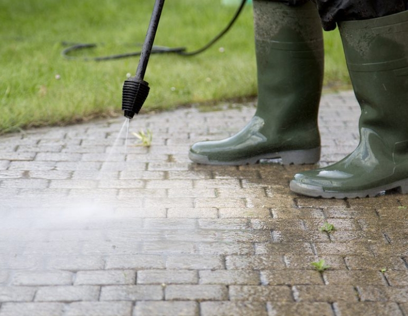 A person in rubber boots is using a power washer.
