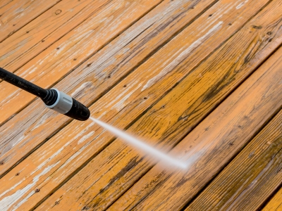 A person uses a power washer to clean the deck.